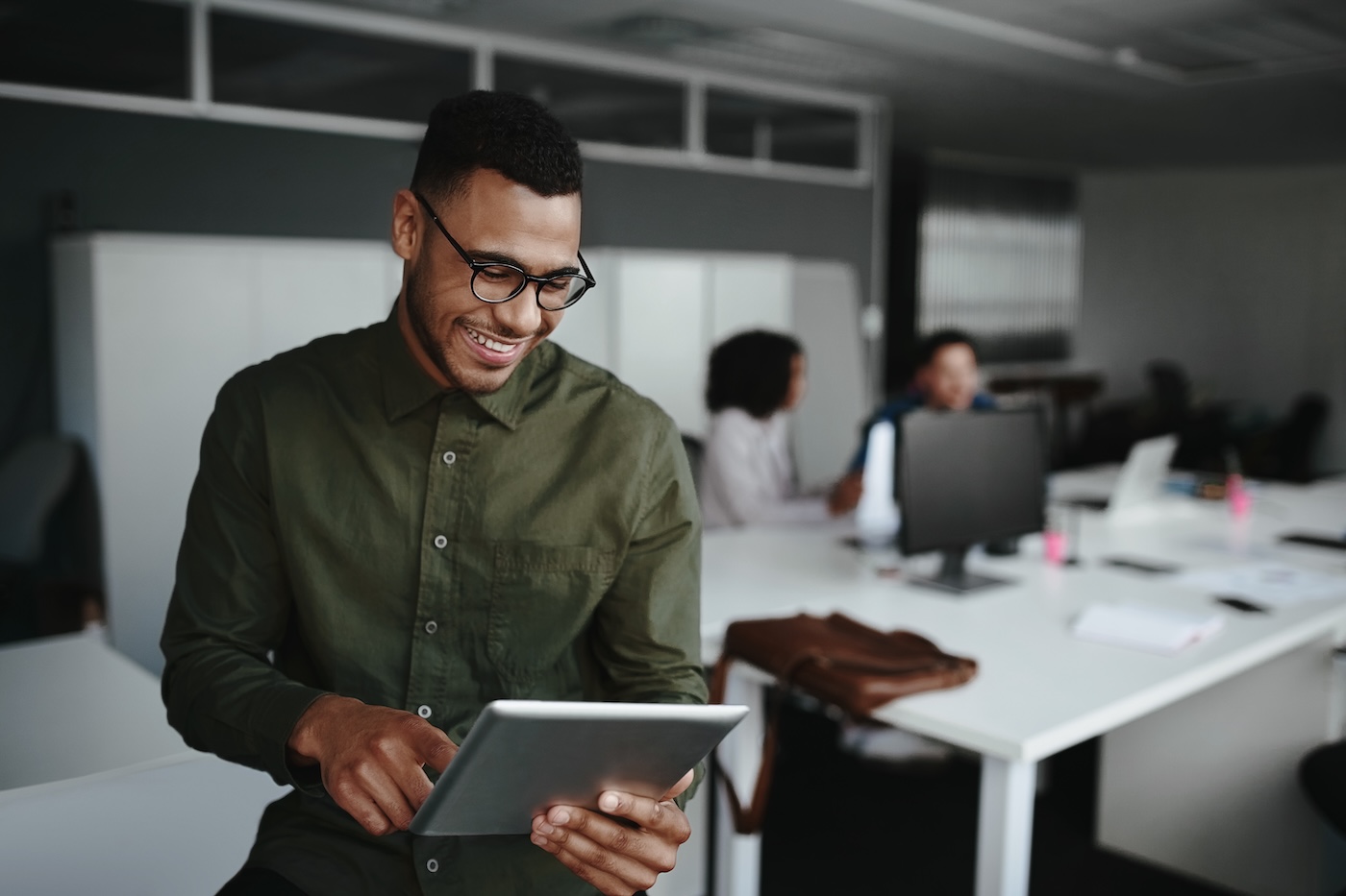 Successful smiling young man in office using digital tablet